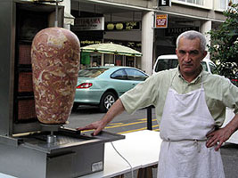 A gentleman looking very French alongside his meat on a stick.  Perhaps he's thinking "Silly American Tourist!"